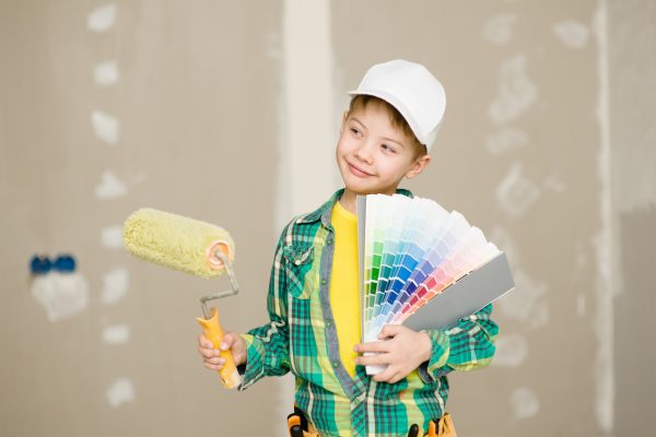 Boy with color samples and paint roller chooses the color of the walls of his room.